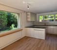 Modern kitchen with white cabinets, black countertop, wooden flooring, and large windows overlooking a garden.