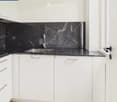Modern kitchen with white cabinets, black marble backsplash, and stainless steel sink.