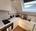 Compact kitchen with white cabinets, light-colored countertops, and a built-in oven. Includes a sink, faucet, blender, and various kitchen items on the counter.