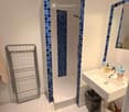 Modern bathroom with white tiles, a bathtub, a sink with a mirror, a towel rack, and a trash bin. Blue mosaic tiles decorate the shower area.