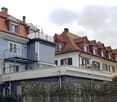 A multi-story residential building with a red-tiled roof, white and blue exterior walls, and multiple balconies. The building features a mix of architectural styles, including modern and traditional elements.