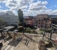 Balcony with wooden decking, metal railing, small table and chairs, and a tree stump as a seat.
