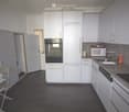 Modern kitchen with white cabinets, granite countertops, and stainless steel appliances. Includes a microwave, oven, sink, and a small table with a chair in the corner.