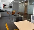 Modern break room with grey cabinets, a microwave, sink, and various seating options including stools and chairs around tables.
