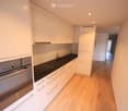 white kitchen with black countertops, wooden cabinets, built-in oven and dishwasher, under-cabinet lighting