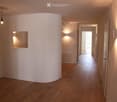 Hallway with wooden floor, white walls, large curved feature wall, recessed lighting, and wall mounted lights