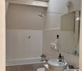 Modern bathroom with a bathtub, toilet, double sink, mirror, and wall-mounted light fixtures. The space features white tiles and a skylight window.