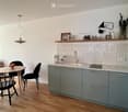 Modern kitchen with grey cabinets, marble countertop, sink, coffee machine, and a small dining area with a round table and chairs.
