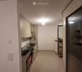 Modern kitchen with tiled floor, white cabinets, stainless steel sink, oven, and a small wooden shelf near the entrance.