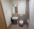 Modern bathroom with a white sink, toilet, mirror, and tiled walls. Includes a shower area with a curtain and various toiletries.