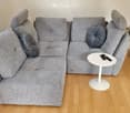 Modern living room with a grey sectional sofa, a white coffee table, and a vase with flowers on the floor.