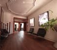 Elegant living room with wooden flooring, a staircase with wooden balusters, two black leather chairs, a large plant in a white pot, and two picture frames on the wall.