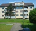 Multi-story residential building with balconies, surrounded by a well-maintained lawn and trees.