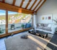Modern living room with a large window offering a scenic view, featuring a grey sofa, coffee table, plush rug, and decorative candle holder.