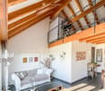 Bright living room with exposed wooden beams, a grey sofa, coffee table, floor lamp, side table, and decorative wall art.