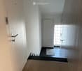 Modern hallway with wooden flooring, white walls, and a small black tiled area leading to a room with a glass door and blinds.