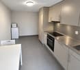 Modern kitchen with light grey cabinets, stainless steel appliances, a white dining table, and a white chair.