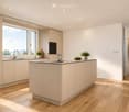 Modern kitchen with light-colored cabinets, a central island, and a wooden dining table. Features include a sink with a modern faucet, an oven, and a view through large windows.