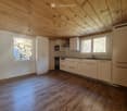 Modern kitchen with light-colored cabinets, wooden flooring, and large windows offering a view of a stone wall outside. Features include a sink, oven, microwave, and ample cabinet space.