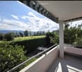 Balcony with a view of a green field, trees, and mountains, featuring a striped awning and a metal railing.