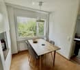 Bright dining area with wooden floor, large window, modern dining table with four chairs, bowl on table, and pendant light fixture.