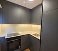 Modern kitchen with dark grey cabinets, white marble countertop, built-in oven, sink, and faucet.