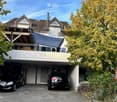 Two-story house with a garage and two parked cars, surrounded by trees.