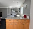 Modern kitchen with grey and wooden cabinets, granite countertop, stainless steel appliances, and a large window.