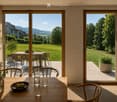 Bright kitchen with large sliding glass doors opening to a patio, wooden dining table with chairs, vase with greenery, bowl of fruit, and glassware.