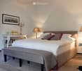 Elegant bedroom with a large bed, nightstands, lamps, a bench at the foot of the bed, and decorative items including a picture frame and candle holder.
