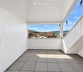 Modern balcony with white wooden paneling, tiled floor, and expansive view of a rural landscape.