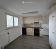 Empty kitchen with white cabinets, a sink, oven, dishwasher, and tiled backsplash. Large windows provide natural light.