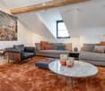 Modern living room with a slanted ceiling, large window, and skylight. Features a grey sofa, armchair, coffee table, and decorative candles.