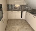 Modern kitchen with white cabinets, granite countertop, tiled floor, and built-in oven.