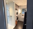 Modern bathroom with a glass-enclosed shower, a stacked washer/dryer unit, a sink with a mirror, and a towel hanging on the wall.