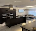 Modern open-plan kitchen and living area with dark wood cabinets, stainless steel appliances, a central island, a sofa, a dining table, and a bowl on the table.