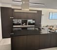 Modern kitchen with dark wood cabinets, black countertop, induction stove, oven, sink, and decorative items on the island.