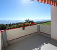 Balcony with white walls, red trim, potted plants, and a scenic mountain view.