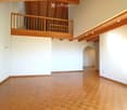 An empty room with wooden flooring and white walls, featuring a wooden balcony level above.
