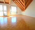Empty room with wooden flooring, white walls, large windows, and a sliding glass door leading to a balcony.