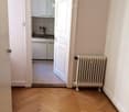 Room has parquet floor, white walls, an open door leading to a kitchen, a radiator