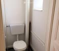 A small bathroom with a white toilet, a small window and a towel hanger.