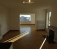 Empty room with wooden flooring, large windows, and a decorative fireplace. Natural light streams in from the windows.