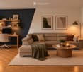 Modern living room with a sectional sofa, coffee table, ottoman, desk with laptop, and various decorative items including plants and picture frames.