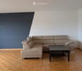 Modern living room with a light-colored sectional sofa, a black coffee table, and wooden flooring.