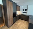 Modern kitchen with wooden and dark grey cabinets, tiled floor, and built-in appliances including an oven and sink.