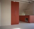 Modern kitchen with red cabinets, a sink, a faucet, and an oven, featuring a large window and a sliding door leading outside.