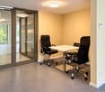 A small, furnished room with a white table and two black office chairs, carpeted floor, and large glass doors leading to an outdoor area.