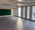 Empty room with grey carpeted floor, large windows, and a green wall panel.