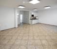 Empty room with tiled floor, white walls, and a small kitchen area featuring white cabinets, a sink, and a microwave. A fireplace is visible on the left side.